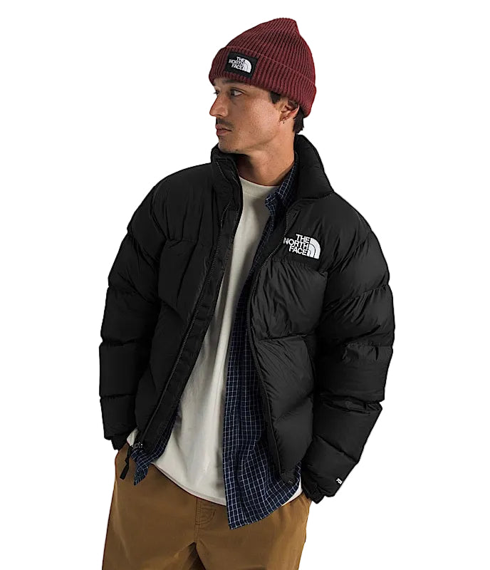 Person wearing a black puffer jacket, white shirt, plaid shirt, brown pants, and maroon beanie with 'The North Face' logo on a white background.